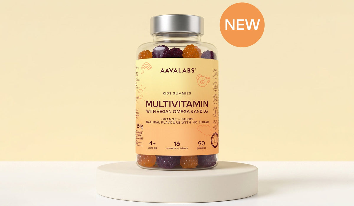 A bottle of AAVALABS Multivitamin gummies with a silver cap and a peach-colored label, displayed on a white round pedestal against a warm beige background with a floating orange 'NEW' badge.