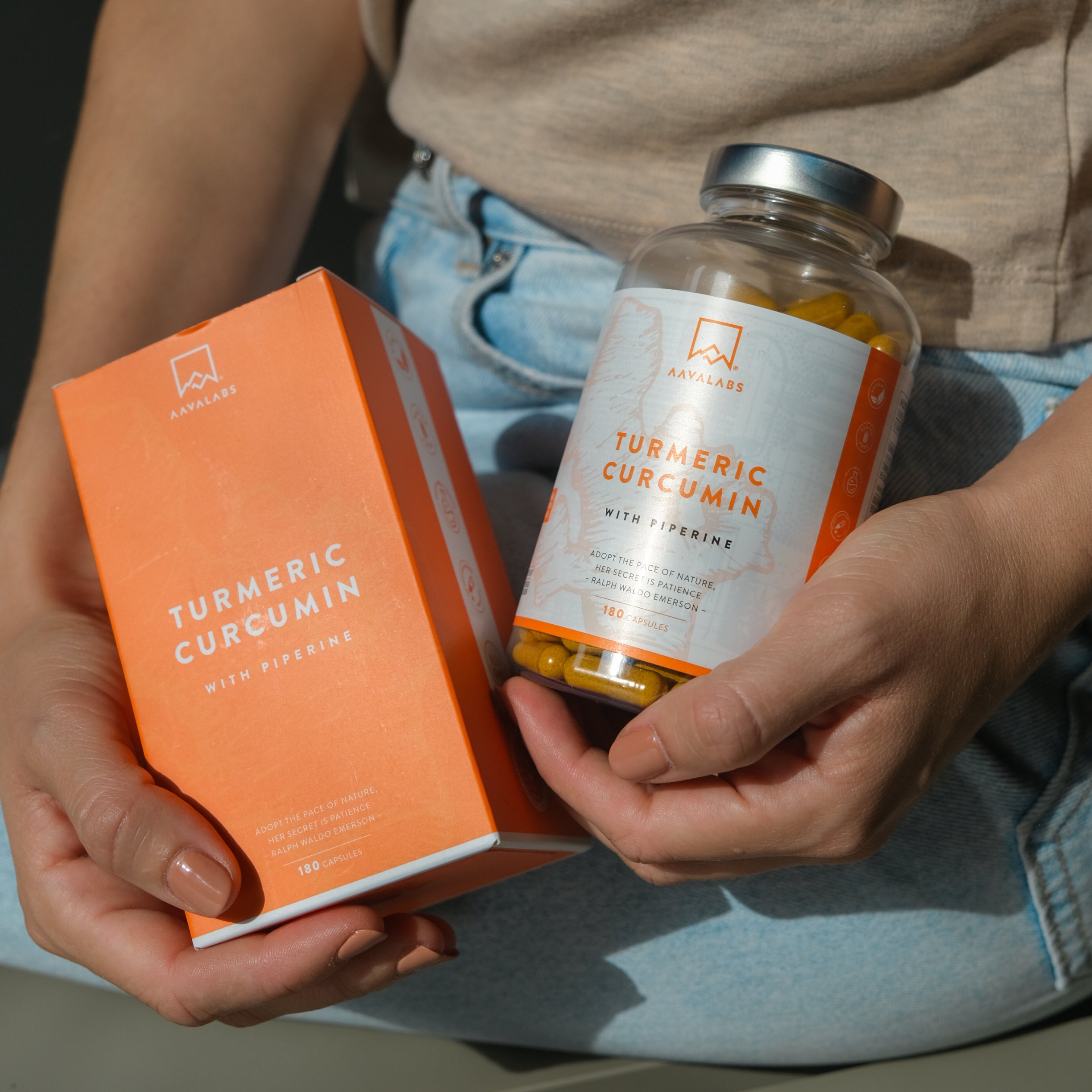 Close-up of a person holding AAVALABS Turmeric Curcumin bottle and box, showcasing the vibrant orange packaging and 180 capsule count