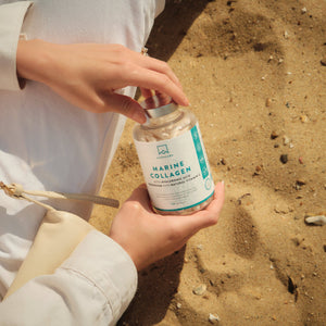 Person holding a bottle of Marine Collagen on sandy ground - AAVALABS