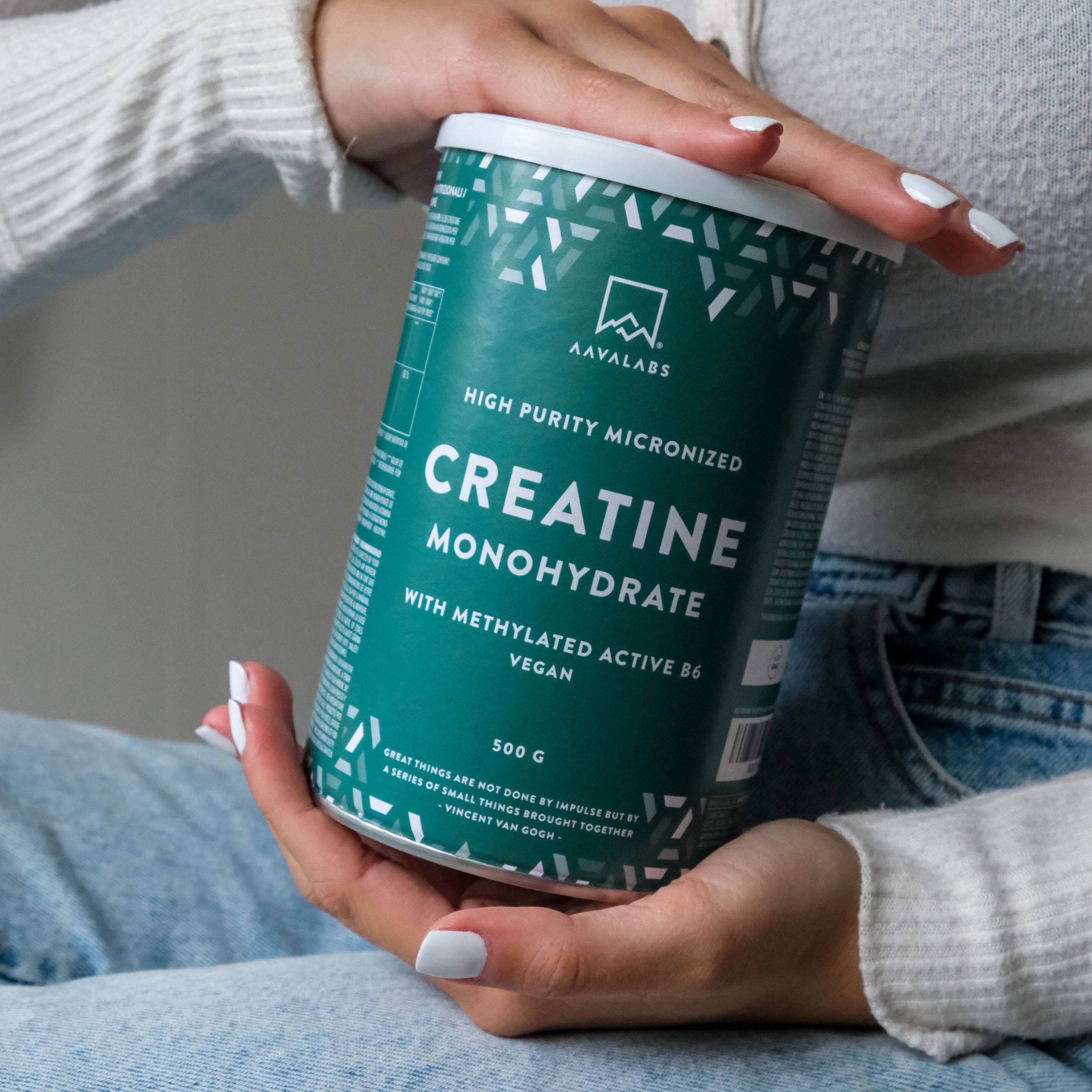 Hands holding a teal AAVALABS Creatine Monohydrate container.