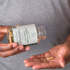 Close-up of hands holding a bottle and capsule of Ginkgo Biloba Complex